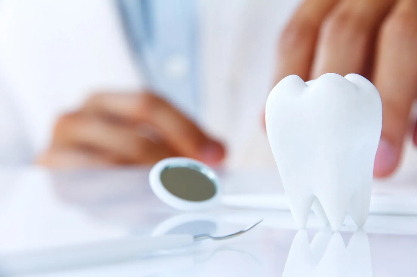A dental mirror beside a tooth model